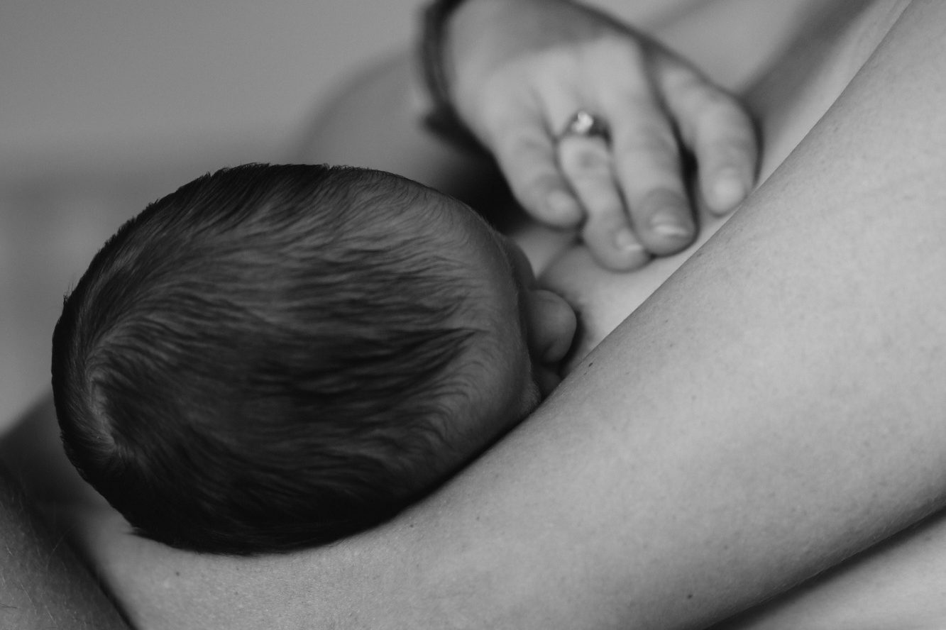 Bildnachweis: wren-meinberg-eWeLO3KR6fo-unsplash Ein Baby stillt an einer Brust.